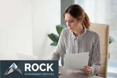 Serious focused businesswoman typing on laptop holding papers preparing report