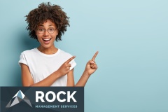Happy smiling woman seller points at upper right corner, advertises item on blank space, has friendly facial expression, wears casual white t shirt, isolated on blue background. Look there, its nice